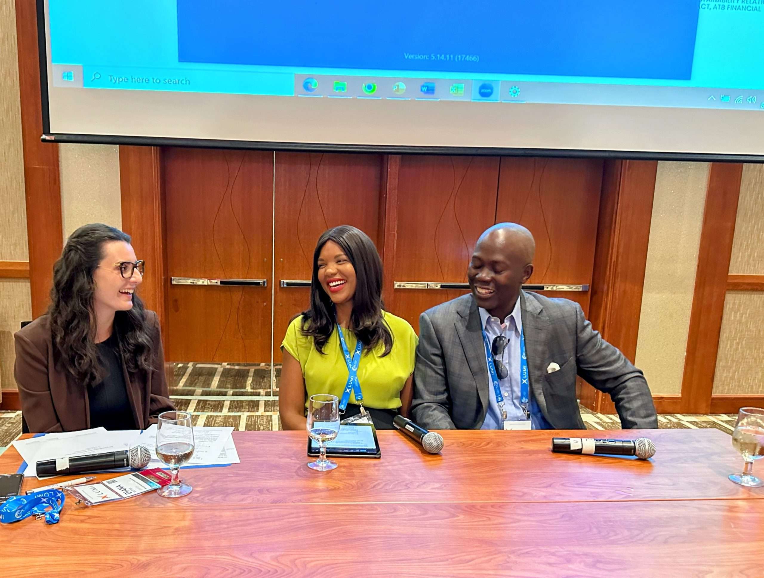 Mante smiles while wearing a neon green short-sleeved blouse and a blue lanyard while sitting between a Black male (right) and a White female (left).