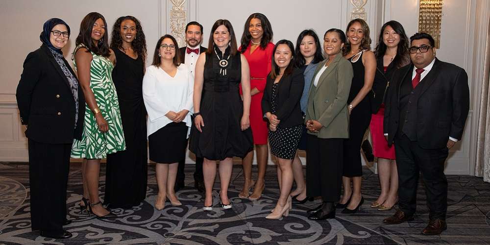 Mante smiles while she stands on the second from left wearing a green and white grass patterned dress amongst a group of people from the OBA Career Accelerator Program.