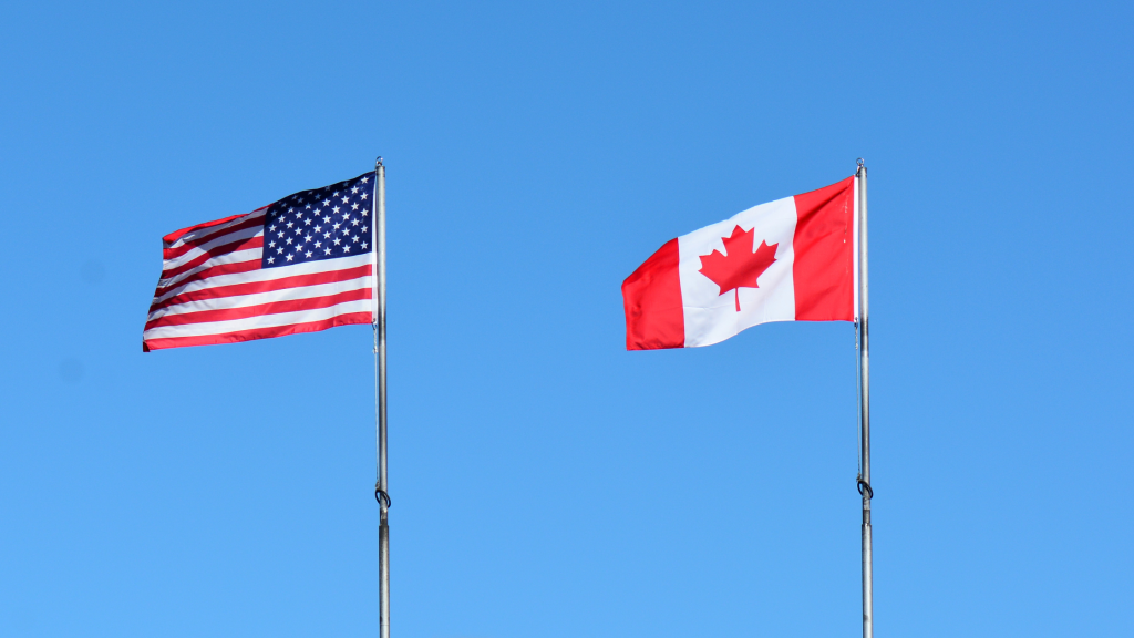 Canada and USA flags on flagpoles with blue sky in the background