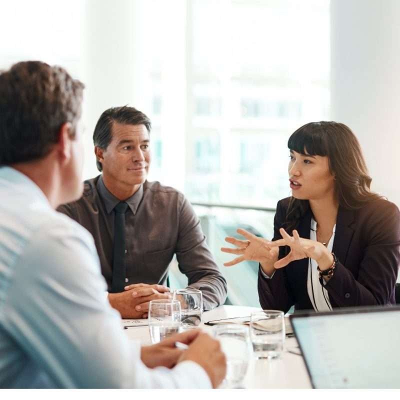 Board meeting with directors seated around a boardroom table while one participant speaks and gestures during a discussion on AI governance in a bright office setting.